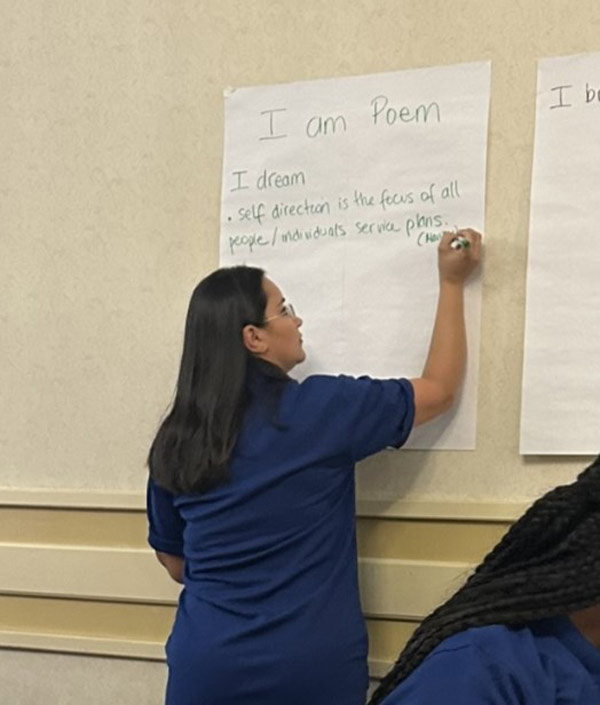 A woman standing and writing on a poster hung on the wall.